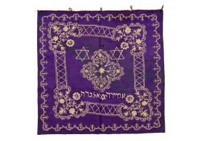 Tik (Torah case) wrapper, purple silk satin with cream cotton embroidery embroidery forming central and corner floral ornaments, later added inscription and motifs of Star of David, dedicated in the name of Amira Allegra.