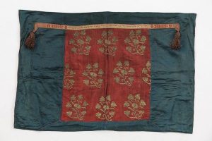 Tik (Torah case) wrapper, cerulean blue silk, wine red silk centrepiece with laid and couched gold embroidery in repeated pattern of blossoming branches, in secondary use, with dedicatory strip in tablet weaving technique, donated by Hannah.