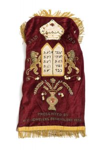Torah mantle, dark red velvet, embroidery and applique work, motifs depicting a flower vase, Tablets of the Covenant with flanking lions and the Corwn of the Torah, dedicated by New York Jewelers' Benevolent Association.