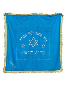 Torah ark curtain for the marriage ceremony, cornflower blue fabric, machine-made, inscribed with one of the blessings of the marriage ceremony, edged with light yellow fringe trim, donated by the American Jewish Joint Distribution Committee to the Patras Congregation, made in the Land of Israel.