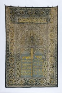 Torah ark curtain, cotton rug in light blue and yellow shades, made from Muslim prayer rug, yellow embroidered inscription, dedicated by Leah to the Old Congregation, Ioannina, in memory of her husband Judah Elijah Jacob, who died in 1932.