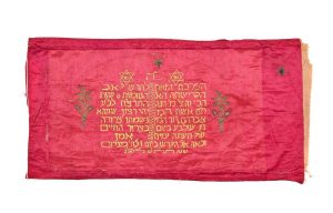 Centrepiece of Torah ark curtain, cherry red silk, with gold embroidery, yellow embroidered inscription, dedicated by Hannah in memory of her husband Abraham David HaLevi, Ioannina (?), who died in 1938.