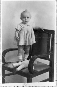 Photograph of a small girl named Dolly at the age of 12 months, standing on a chair, Belgrade, 02/01/1938