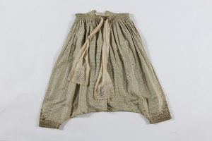 Woman's baggy trousers, cream cotton with small gold and green floral pattern, sash fastening, cream cotton sash with floral embroidered ends, braided gold cord embroidery at ankle cuffs, probably belonged to a member of the the local Jewish community.