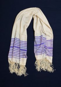 Prayer shawl, cream silk with iris blue stripes along the edge, with white square corner reinforcements.