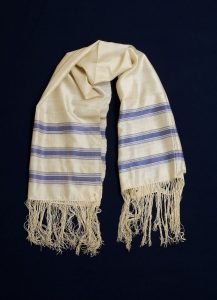 Prayer shawl, cream silk with blue stripes along the edge.