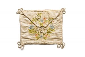 Envelope bag for prayer shawl, cream silk edged with cream cord, embroidered floral wreath in green, blue and salmon enclosing owner's name, belonged to Daniel Abraham Esdra, Trikala.