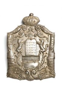 Silver repousse Torah shield in cartouche shape with Jewish motifs.