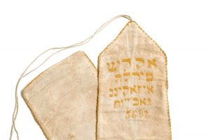 Binder for the Torah scroll, narrow white linen band with lining, light orange embroidered inscription, dedicated by Perla Isaakino (?), Athens.