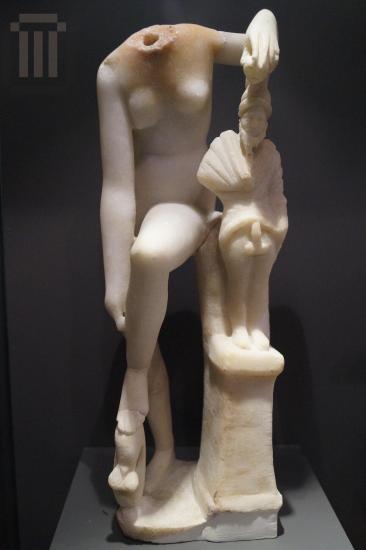 Marble statuette of Aphrodite wearing her sandals, leaning on a small pillar with Priapus