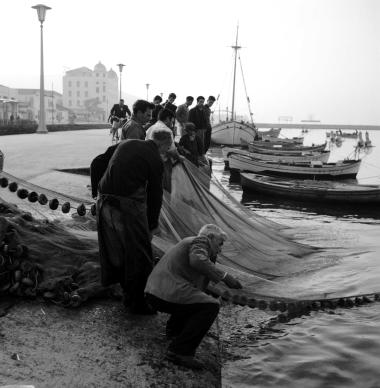 Το άπλωμα των διχτυών στην παραλία. Στο βάθος οι καπναποθήκες Παπαστράτου