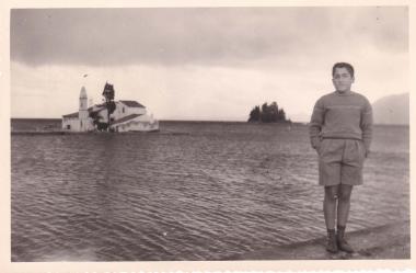 Νεαρό αγόρι μπροστά από τη νησίδα της Βλαχέρνας (με το εκκλησάκι της Παναγίας των Βλαχερνών) και το Ποντικονήσι στην Κέρκυρα.