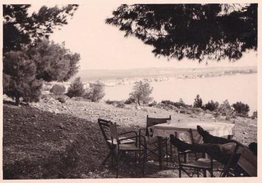 Παραλία στο Λουτράκι, με τραπεζοκαθίσματα καταστήματος στη σκιά των δέντρων.