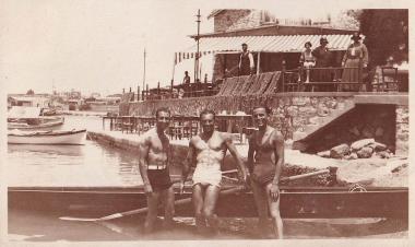 Τρεις άνδρες με μαγιό μπροστά σε λέμβο, δίπλα σε παραλιακό κατάστημα του Καλαμακίου.