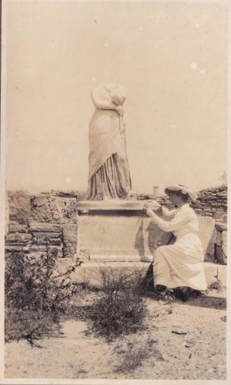 Γυναίκα καθισμένη μπροστά σε ακέφαλο γυναικείο άγαλμα στον αρχαιολογικό χώρο της Δήλου.