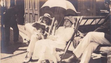 Άνδρας με βιβλίο και γυναίκα με ομπρέλα, καθισμένοι σε πολυθρόνες στο κατάστρωμα πλοίου.