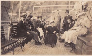 Συντροφιά ανδρών και γυναικών στο κατάστρωμα πλοίου, που βρίσκεται στα νερά της Καλντέρας, κάτω από τα Φηρά της Σαντορίνης (Θήρας).