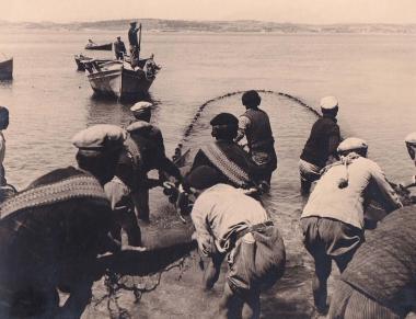 Ψαράδες των Σπετσών απλώνουν τα δίχτυα τους στη θάλασσα∙ στο βάθος ψαρόβαρκες.