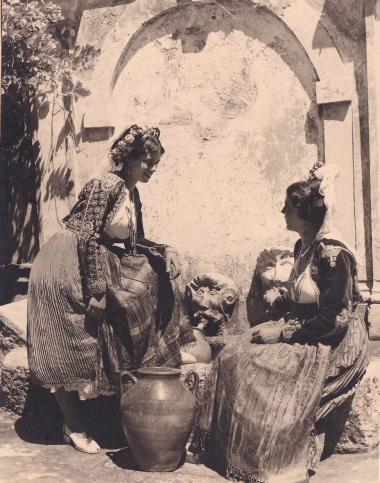 Γυναίκες της Κέρκυρας, με παραδοσιακές ενδυμασίες και πιθάρια, μπροστά σε δημόσια κρήνη.