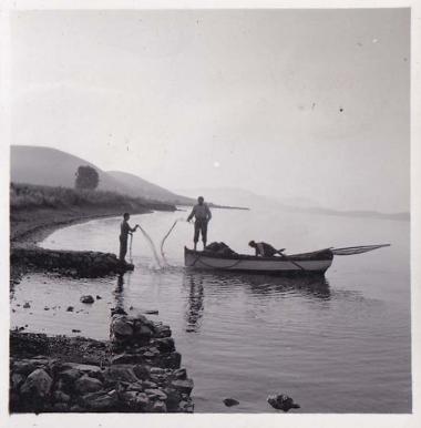 Ψαράδες σε βάρκα απλώνουν δίχτυα σε ακτή.