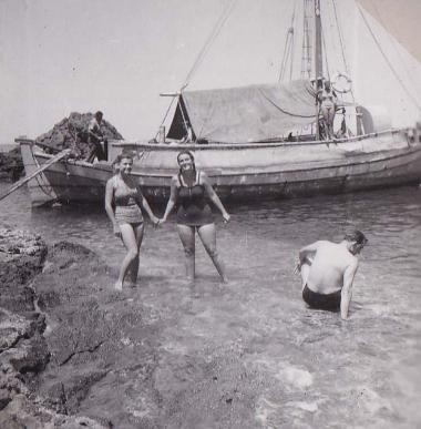 Άνδρας και δύο γυναίκες στη θάλασσα, κοντά σε καΐκι δεμένο σε παραλία της Δήλου.