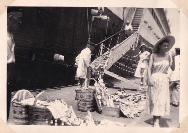 Πλανόδιος πωλητής τουριστικών ενθυμίων μπροστά από το ατμόπλοιο Providence στο λιμάνι του Πειραιά, κοντά στο Τελωνείο. Το πλοίο ναυπηγήθηκε στη Γαλλία και καθελκύστηκετο 1914∙ αρχικά ανήκε στην εταιρεία Cyprien Fabre και, από το 1932, στην Messageries Maritimes. Αποσύρθηκε και διαλύθηκε το 1951-1952.