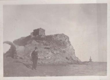 Άνδρας στέκεται μπροστά στη νησίδα με τα ερείπια του ενετικού κάστρου (ή Κάτω Κάστρου), στη Χώρα της Άνδρου. Η νησίδα συνδέεται με τη στεριά της Χώρας μέσω της πέτρινης γέφυρας που διακρίνεται στα αριστερά.